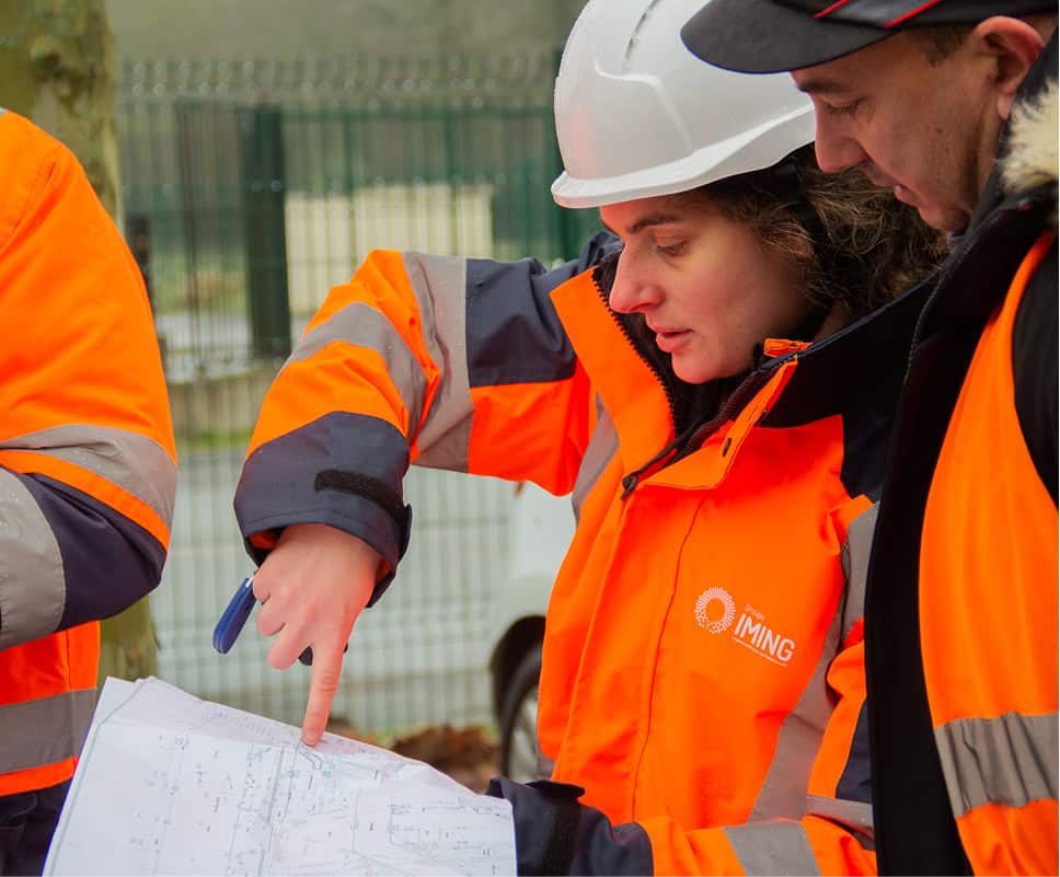 Ingénieurs en sécurité sur un site de construction avec plans et équipements de protection.